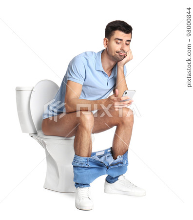 Emotional man with smartphone sitting on toilet bowl, white background 98000844