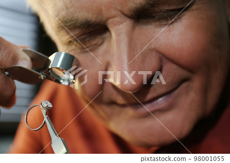 Professional jeweler evaluating beautiful ring in workshop, closeup Professional jeweler evaluating beautiful ring in workshop, closeup 98001055