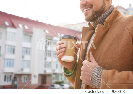 Man with cup of coffee on city street in morning, closeup Man with cup of coffee on city street in morning, closeup 98001063
