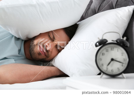 Emotional man covering ears with pillows at home in morning Emotional man covering ears with pillows at home in morning 98001064
