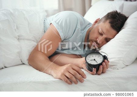 Man sleeping with alarm clock at home in morning Man sleeping with alarm clock at home in morning 98001065