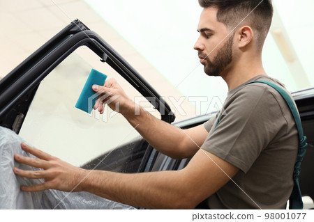 Worker washing tinted car window in workshop Worker washing tinted car window in workshop 98001077
