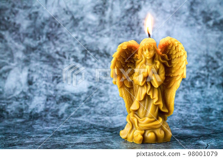 Beeswax praying angel candle on stone background 98001079