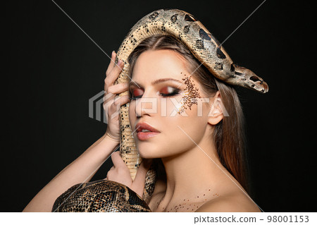 Beautiful woman with boa constrictor on black background 98001153