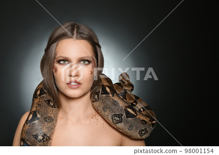 Beautiful woman with boa constrictor on dark background. Space for text 98001154