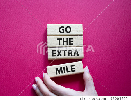 Go the extra mile symbol. Wooden blocks with words Go the extra mile. Beautiful red background. Businessman hand. Business and Go the extra mile concept. Copy space. 98001501