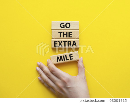 Go the extra mile symbol. Wooden blocks with words Go the extra mile. Beautiful yellow background. Businessman hand. Business and Go the extra mile concept. Copy space. 98001515