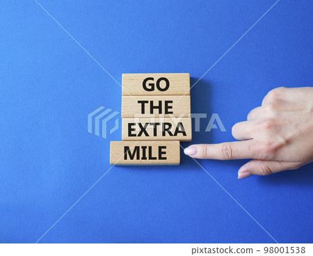 Go the extra mile symbol. Wooden blocks with words Go the extra mile. Businessman hand. Beautiful blue background. Business and Go the extra mile concept. Copy space. 98001538