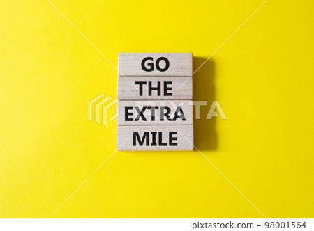 Go the extra mile symbol. Wooden blocks with words Go the extra mile. Beautiful yellow background. Business and Go the extra mile concept. Copy space. 98001564