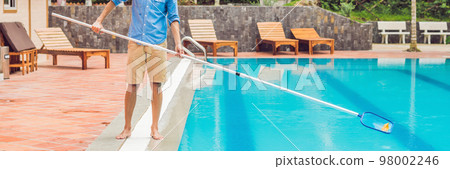 Cleaner of the swimming pool . Man in a blue shirt with cleaning equipment for swimming pools, sunny BANNER, long format 98002246