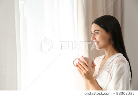 Young woman with cup of coffee near window. Lazy morning 98002385