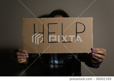Young woman with sign HELP near beige wall. Domestic violence concept 98002389