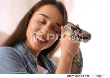 Young woman with her boa constrictor at home, focus on hand 98002392