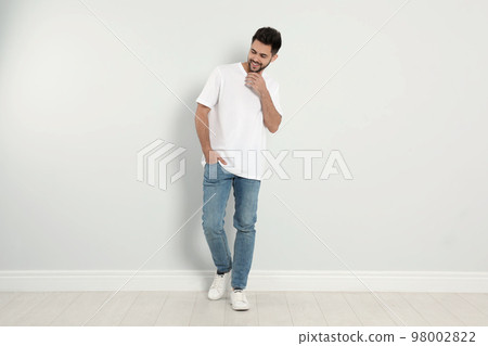 Young man in stylish jeans near light wall 98002822