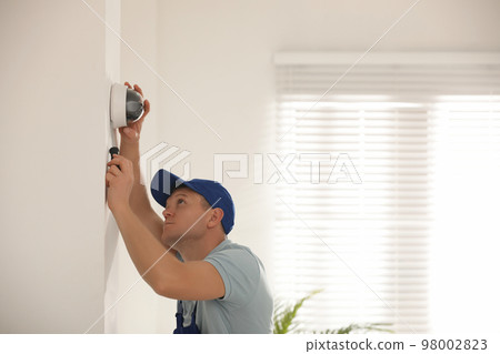 Technician installing CCTV camera on wall indoors 98002823