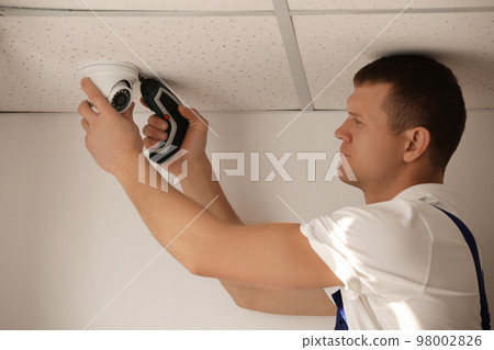 Technician installing CCTV camera on ceiling indoors 98002826