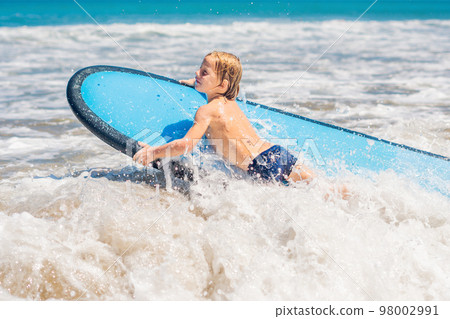 Happy baby boy - young surfer ride on surfboard with fun on sea waves. Active family lifestyle, kids outdoor water sport lessons and swimming activity in surf camp. Summer vacation with child 98002991