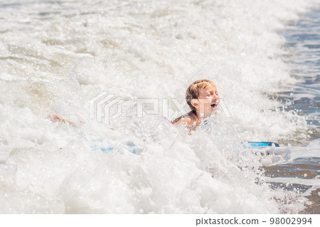 Happy baby boy - young surfer ride on surfboard with fun on sea waves. Active family lifestyle, kids outdoor water sport lessons and swimming activity in surf camp. Summer vacation with child 98002994