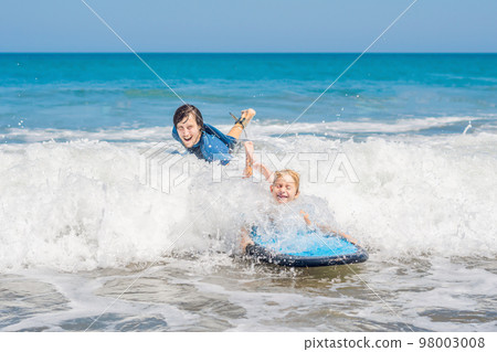 Father teaching his young son how to surf in the sea on vacation or holiday. Travel and sports with children concept Father teaching his young son how to surf in the sea on vacation or holiday. Travel and sports with children concept 98003008