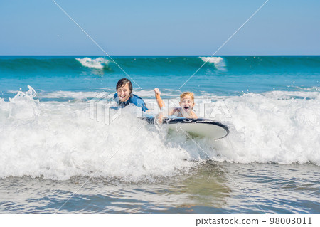 Father teaching his young son how to surf in the sea on vacation or holiday. Travel and sports with children concept 98003011