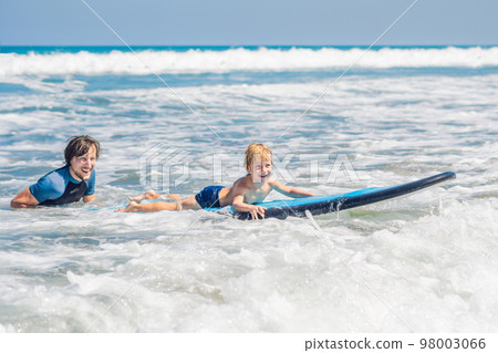 Father teaching his young son how to surf in the sea on vacation or holiday. Travel and sports with children concept 98003066