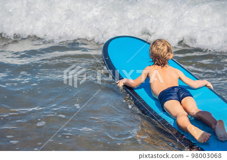 Happy baby boy - young surfer ride on surfboard with fun on sea waves. Active family lifestyle, kids outdoor water sport lessons and swimming activity in surf camp. Summer vacation with child Happy baby boy - young surfer ride on surfboard with fun on sea waves. Active family lifestyle, kids outdoor water sport lessons and swimming activity in surf camp. Summer vacation with child 98003068