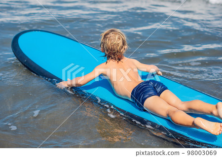 Happy baby boy - young surfer ride on surfboard with fun on sea waves. Active family lifestyle, kids outdoor water sport lessons and swimming activity in surf camp. Summer vacation with child 98003069