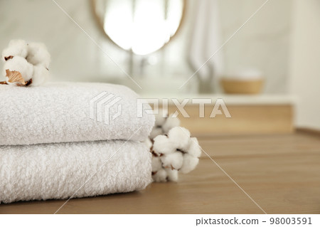Stack of clean towels and cotton flowers on wooden table in bathroom. Space for text 98003591