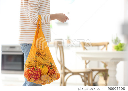 Woman with net bag full of fruits and vegetables in kitchen, closeup. Space for text Woman with net bag full of fruits and vegetables in kitchen, closeup. Space for text 98003608