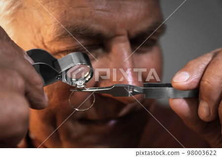 Professional jeweler evaluating beautiful ring, closeup view Professional jeweler evaluating beautiful ring, closeup view 98003622