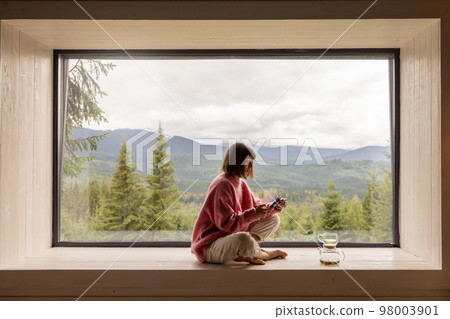 Woman rests in house with scenic views in mountains Woman rests in house with scenic views in mountains 98003901