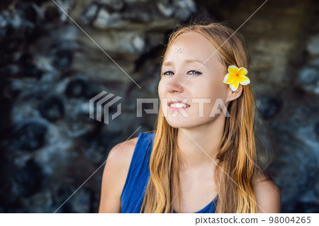 Woman is a tourist in Bali. The ritual of ablution with holy water and on her forehead prikleeli rice and put the flower ear Woman is a tourist in Bali. The ritual of ablution with holy water and on her forehead prikleeli rice and put the flower ear 98004265
