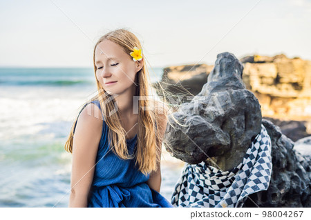 Woman is a tourist in Bali. The ritual of ablution with holy water and on her forehead prikleeli rice and put the flower ear Woman is a tourist in Bali. The ritual of ablution with holy water and on her forehead prikleeli rice and put the flower ear 98004267