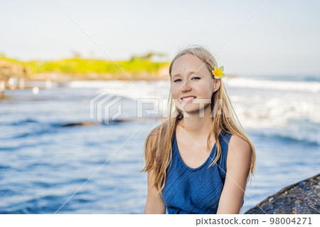 Woman is a tourist in Bali. The ritual of ablution with holy water and on her forehead prikleeli rice and put the flower ear Woman is a tourist in Bali. The ritual of ablution with holy water and on her forehead prikleeli rice and put the flower ear 98004271
