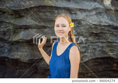 Woman is a tourist in Bali. The ritual of ablution with holy water and on her forehead prikleeli rice and put the flower ear 98004274