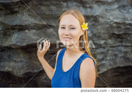 Woman is a tourist in Bali. The ritual of ablution with holy water and on her forehead prikleeli rice and put the flower ear 98004275