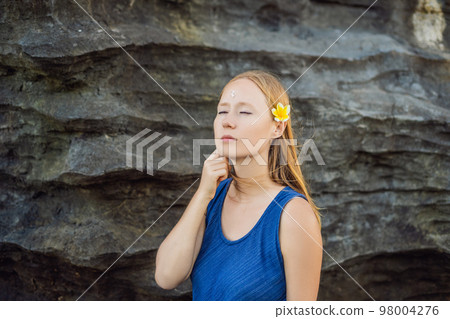 Woman is a tourist in Bali. The ritual of ablution with holy water and on her forehead prikleeli rice and put the flower ear 98004276