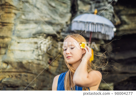 Woman is a tourist in Bali. The ritual of ablution with holy water and on her forehead prikleeli rice and put the flower ear 98004277