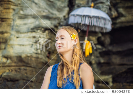 Woman is a tourist in Bali. The ritual of ablution with holy water and on her forehead prikleeli rice and put the flower ear Woman is a tourist in Bali. The ritual of ablution with holy water and on her forehead prikleeli rice and put the flower ear 98004278