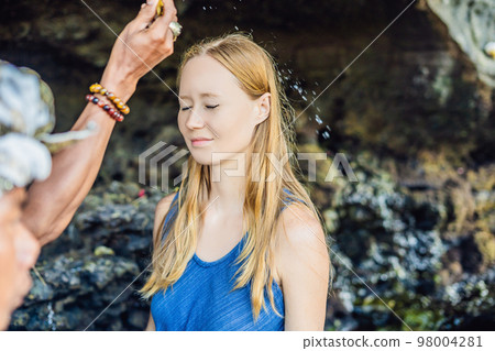Woman is a tourist in Bali. The ritual of ablution with holy water and on her forehead prikleeli rice and put the flower ear 98004281