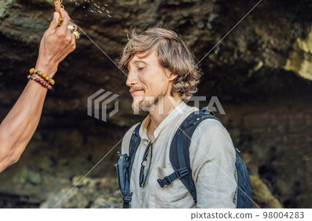 Man is a tourist in Bali. The ritual of ablution with holy water and on her forehead prikleeli rice and put the flower ear 98004283
