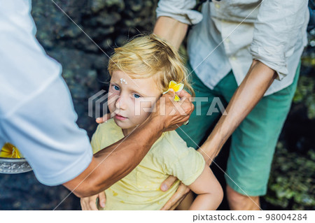 Boy is a tourist in Bali. The ritual of ablution with holy water and on her forehead prikleeli rice and put the flower ear Boy is a tourist in Bali. The ritual of ablution with holy water and on her forehead prikleeli rice and put the flower ear 98004284