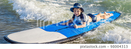 Happy baby boy - young surfer ride on surfboard with fun on sea waves. Active family lifestyle, kids outdoor water sport lessons and swimming activity in surf camp. Summer vacation with child BANNER Happy baby boy - young surfer ride on surfboard with fun on sea waves. Active family lifestyle, kids outdoor water sport lessons and swimming activity in surf camp. Summer vacation with child BANNER 98004313