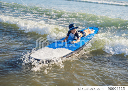 Happy baby boy - young surfer ride on surfboard with fun on sea waves. Active family lifestyle, kids outdoor water sport lessons and swimming activity in surf camp. Summer vacation with child 98004315