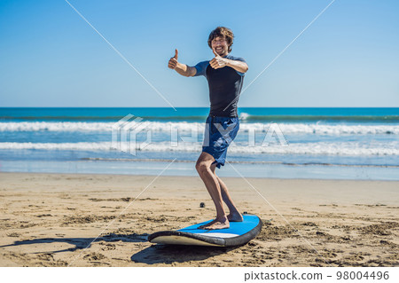 Young man surfer training before go to lineup on a sand beach. Learning to surf. Vacation concept. Summer holidays. Tourism, sport 98004496