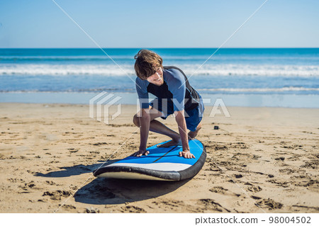 Young man surfer training before go to lineup on a sand beach. Learning to surf. Vacation concept. Summer holidays. Tourism, sport 98004502