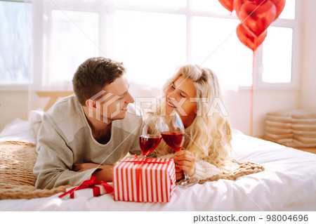 Beautiful young couple at home celebrating Valentine's Day. Lovers give each other gifts. 98004696