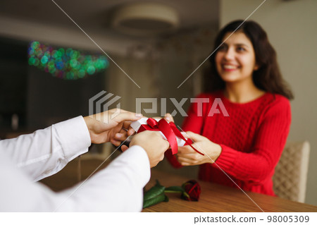 Man gives to his woman a gift box with red ribbon. Hands of man gives surprise gift box for girl. Man gives to his woman a gift box with red ribbon. Hands of man gives surprise gift box for girl. 98005309