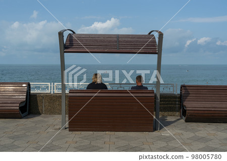 A man and a woman are sitting on a bench in front of the sea. A man and a woman are sitting on a bench in front of the sea. 98005780