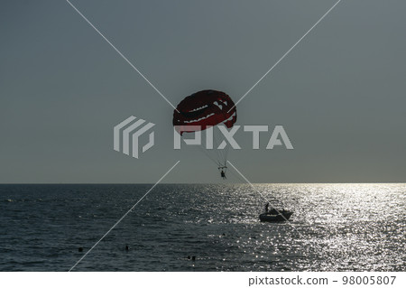 A man soars on a parachute over the sea behind a boat. 98005807